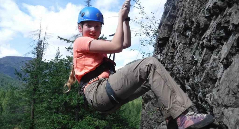 an outward bound student sits back on the ropes suspending them while rock climbing